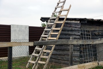 two wooden stairs stand at the gray wall of the barn behind the fence