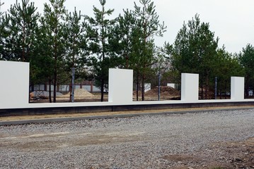 white unfinished concrete fence on the street by the road in front of pine trees