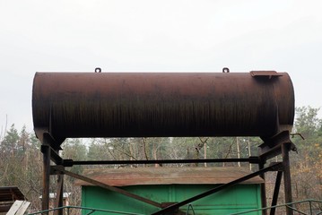 one brown rusty iron tank stands against a gray sky