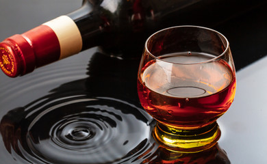 Bottle of red wine with wineglass. Water splash and droplet on the black reflection.