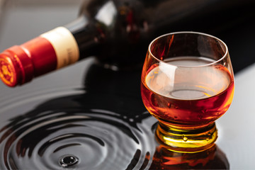 Bottle of red wine with wineglass. Water splash and droplet on the black reflection.