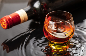 Bottle of red wine with wineglass. Water splash and droplet on the black reflection.