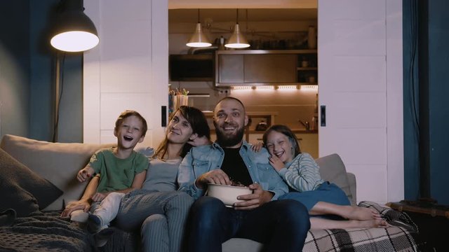 Happy smiling young Caucasian family with two kids watch movies at home on couch, laugh together. Entertainment concept.