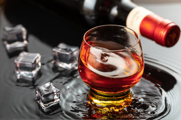 Bottle of red wine with wineglass. Water splash and droplet on the black reflection.