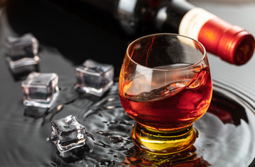 Bottle of red wine with wineglass. Water splash and droplet on the black reflection.