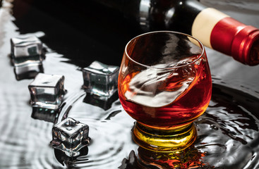 Bottle of red wine with wineglass. Water splash and droplet on the black reflection.