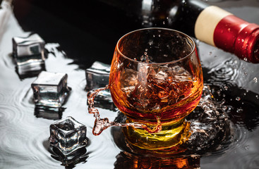 Bottle of red wine with wineglass. Water splash and droplet on the black reflection.