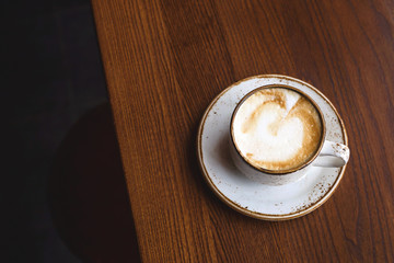 Cappuccino in rustic cup and dish on a brown coffee shop table. Top view, flat lay.
