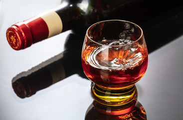Bottle of red wine with wineglass. Water splash and droplet on the black reflection.
