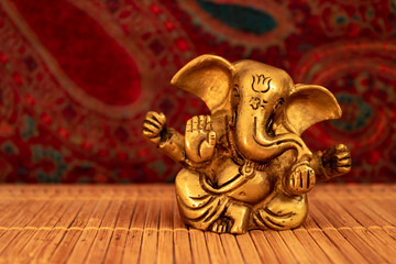 Golden Ganesha statue on bamboo mat and oriental background, close up