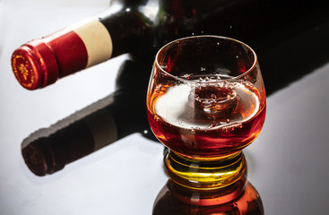 Bottle of red wine with wineglass. Water splash and droplet on the black reflection.