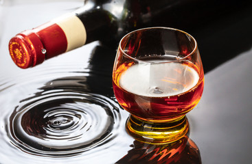 Bottle of red wine with wineglass. Water splash and droplet on the black reflection.