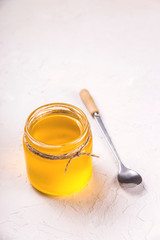 Ghee or clarified butter in a glass jar on a neutral textured background next to a spoon.
