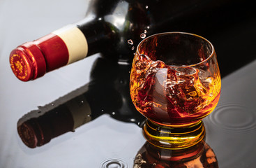 Bottle of red wine with wineglass. Water splash and droplet on the black reflection.