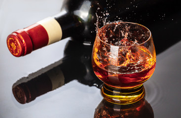 Bottle of red wine with wineglass. Water splash and droplet on the black reflection.