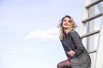 A young Caucasian girl in an autumn checkered coat laughing and looking down at the camera against a blue sky.
