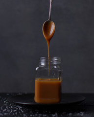 Spoon drizzling salted caramel sauce into a clear glass jar