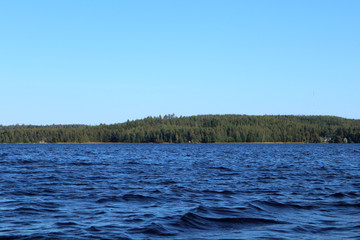 Blue water clear sky sunny day on finnish lake water waves close up. Beauty of nature skyline and forest with deep colored water. Photo from boat