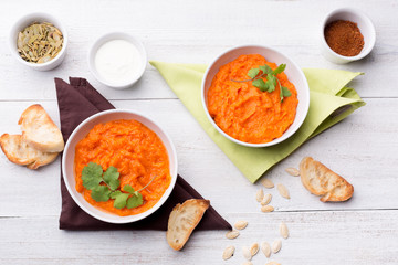 Two plates with a side dish of pumpkin with croutons, sour cream, pumpkin seeds, cilantro and spices on a white wooden background.