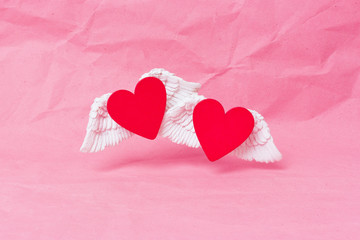 Happy valentines day banner. A red wooden heart with white voluminous wings soars over a pink crumpled paper background. Minimalism. Place for text