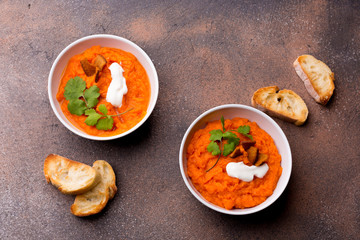 Two plates with a side dish of pumpkin with croutons, sour cream, pumpkin seeds, cilantro and spices on a white wooden background.