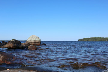 Stones granite coast of island on finish lake on bright sunny summer day blue sky and water landscape view scenic nature background
