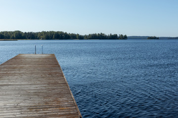 Wooden swimming dock pier with metal ladder on calm blue lake sunny day on nature finland idyllic...