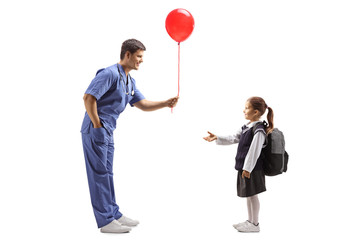Obraz na płótnie Canvas Doctor in a blue uniform giving a balloon to a little schoolgirl