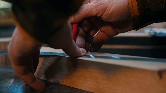 Carpentry industry - a woodworker making marks for cutting on the wooden detail with a pencil and yardstick