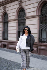 Fototapeta premium Autumn fashion outdoor. The girl in fashionable stylish white shirt , pants, jacket and sunglasses, autumnal lifestyle on the background of blurry yellow-green trees in the park. Vertical