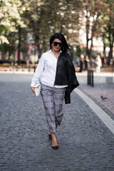 Obraz premium Autumn fashion outdoor. The girl in fashionable stylish white shirt , pants, jacket and sunglasses, autumnal lifestyle on the background of blurry yellow-green trees in the park. Vertical