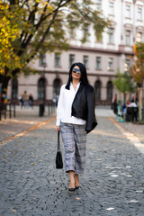 Autumn fashion outdoor. The girl in fashionable stylish white shirt , pants, jacket and sunglasses, autumnal lifestyle on the background of blurry yellow-green trees in the park. Vertical