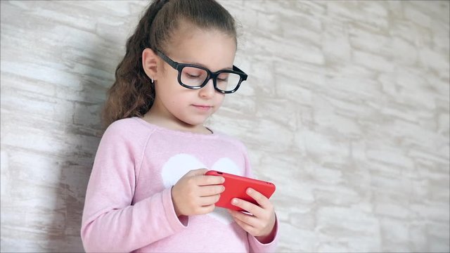 Cute baby entertaining with a mobile phone or tablet. Little girl spends her free time playing a mobile game and crushes a bright screen with her hand. Concept: Happy Childhood, Games for children.