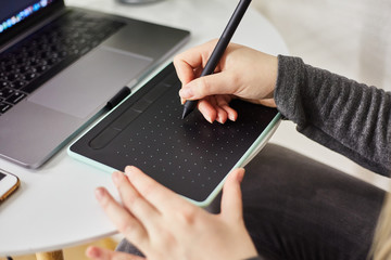 Kaliningrad, Russia - October 27, 2019: A young girl draws on a graphics tablet. Freelancer works in a cafe