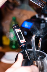 soft focus of soft focus of barista hands measure hot water temperature with in silver jug in cafe