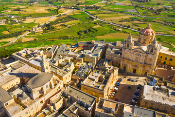 Fototapeta na wymiar The main church and square in Mdina city - old capital of Malta. Aerial nature landscape, sunny day, blue sly, winter, a lot of green grass, field on background. Malta 