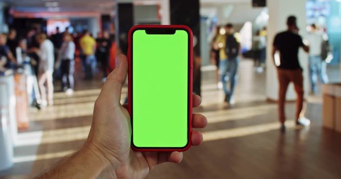 Male hand turning around tapping blank green screen smartphone mobile close-up. Chroma-key display touchscreen. Checking news. Business application online. Social media. Mock-up. Conference meeting.