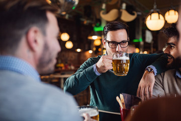 Handsome man drinking beer in pub with his friends