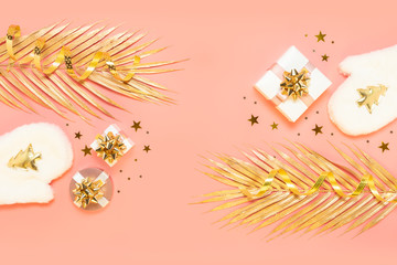 Obraz premium New year Christmas Stylish festive decorations concept, Golden palm leaves, white mittens, gift boxes, starry confetti, candles on pink background. Flat lay, copy space. Backdrop for greeting card