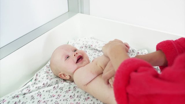 Mother is doing physical exercises with baby-boy's hands on the changing table before swimming in the swimming pool. Adorable boy is smiling