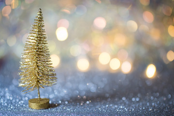 A small gold Christmas tree on a silver surface with defocused background with bokeh lights.