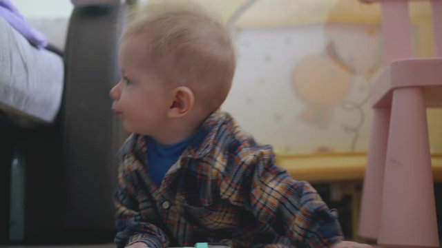 funny little baby in checkered shirt scrawls and leans on soft bed on wooden floor in children room close view