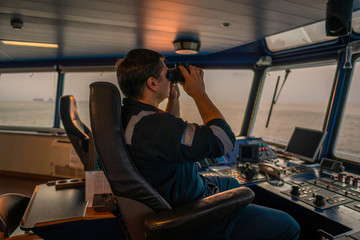 Navigational officer lookout on navigation watch looking through binoculars. Marine industry. COLREG collision regulations