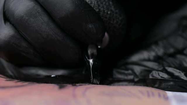 Close up tattoo artist demonstrates the process of getting black tattoo with paint on back of a client