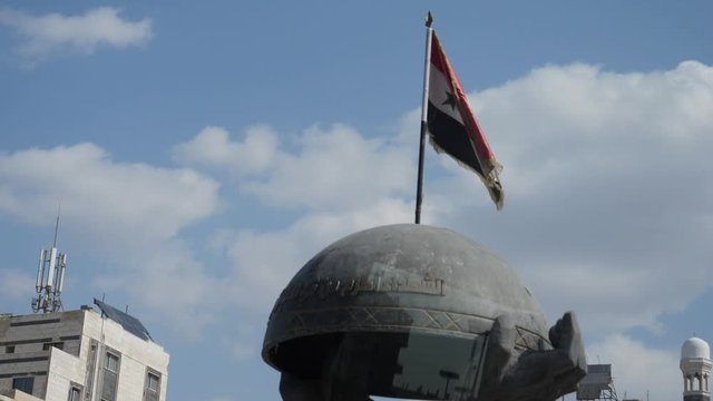 Slow motion shot moving closer to a Syrian flag waving on top of a monument in Homs City