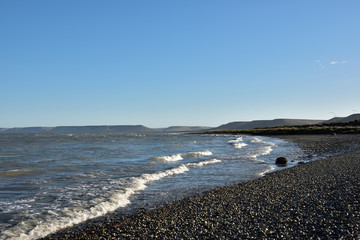 vista de playa con olas de marea subiendo y colinas bajo el cielo azul