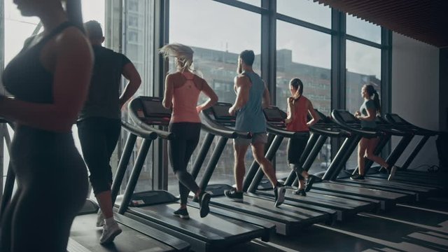 Beautiful Athletic Woman Uses Smartphone Walks Through Fitness Club Gym. Using Social Media, Posting Pictures, Communicating, Checking Email. In the Background Sports People Running on Treadmills
