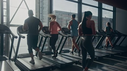 Beautiful Athletic Woman Uses Smartphone Walks Through Fitness Club Gym. Using Social Media, Posting Pictures, Communicating, Checking Email. In the Background Sports People Running on Treadmills - Powered by Adobe