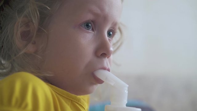 tired little girl in yellow shirt undergoes medical procedure with inhaler in light room extreme close view
