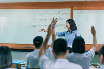 An Asian female teacher is teaching Japanese. The meaning of texts are "Mr. Suriya bought a shirt for the teacher, Mr Ittithep taught me Japanese, I have been taught Japanese from Mr Athithep".